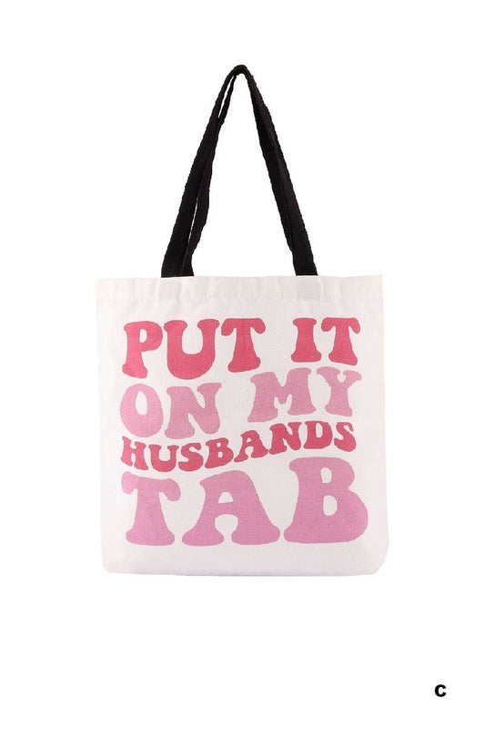 Tote bag with pink text 'PUT IT ON MY HUSBAND'S TAB' on a white background