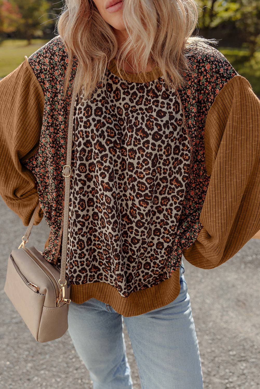 Person wearing a leopard print top with brown sleeves and light blue jeans, holding a beige handbag.