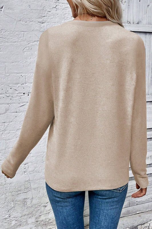 Person wearing a beige sweater and blue jeans against a textured white wall.