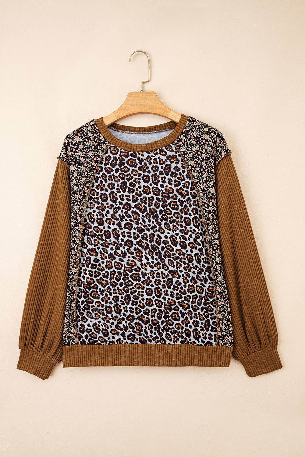 Leopard print sweater with brown sleeves on a hanger against a beige background