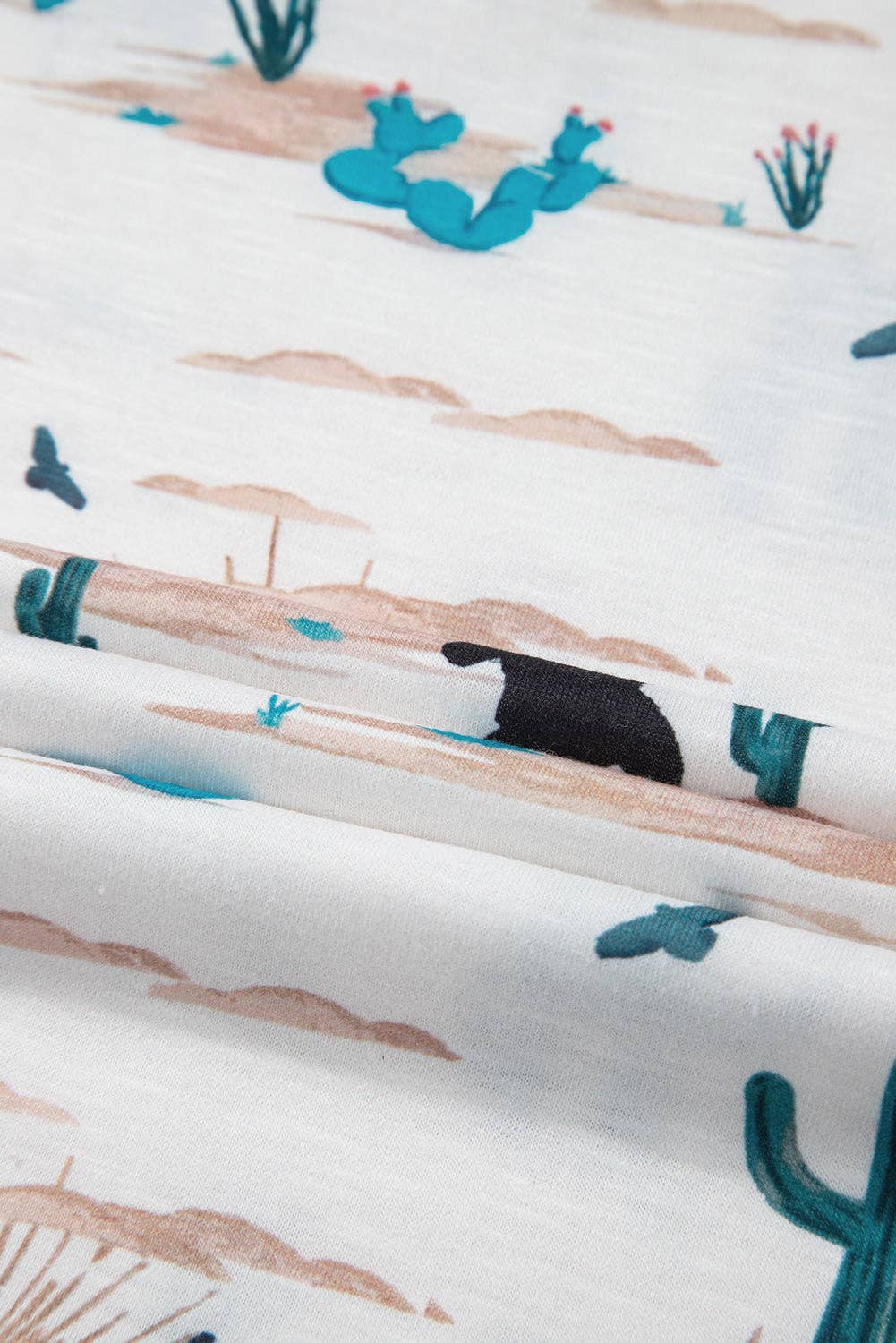 Close-up of fabric with desert-themed print featuring cacti and sand dunes.