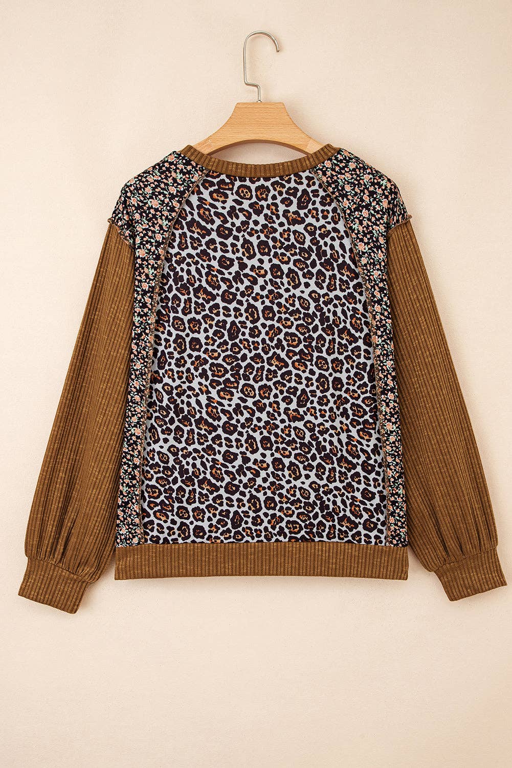Leopard print sweater with brown sleeves on a hanger against a beige background
