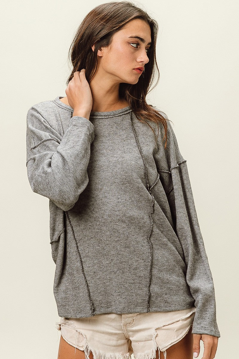 Woman wearing a gray sweatshirt and beige shorts on a plain background